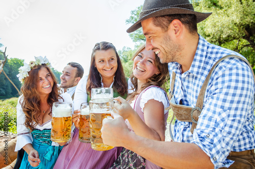 Freunde in bayerischen Tracht feiern an der Isar und trinken Bier. Oktoberfest München