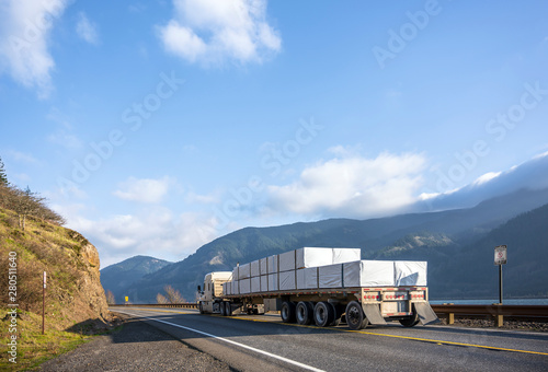 Big rig low cab semi truck transporting covered cargo on flat bed semi trailer running on the road in Columbia Gorge area photo