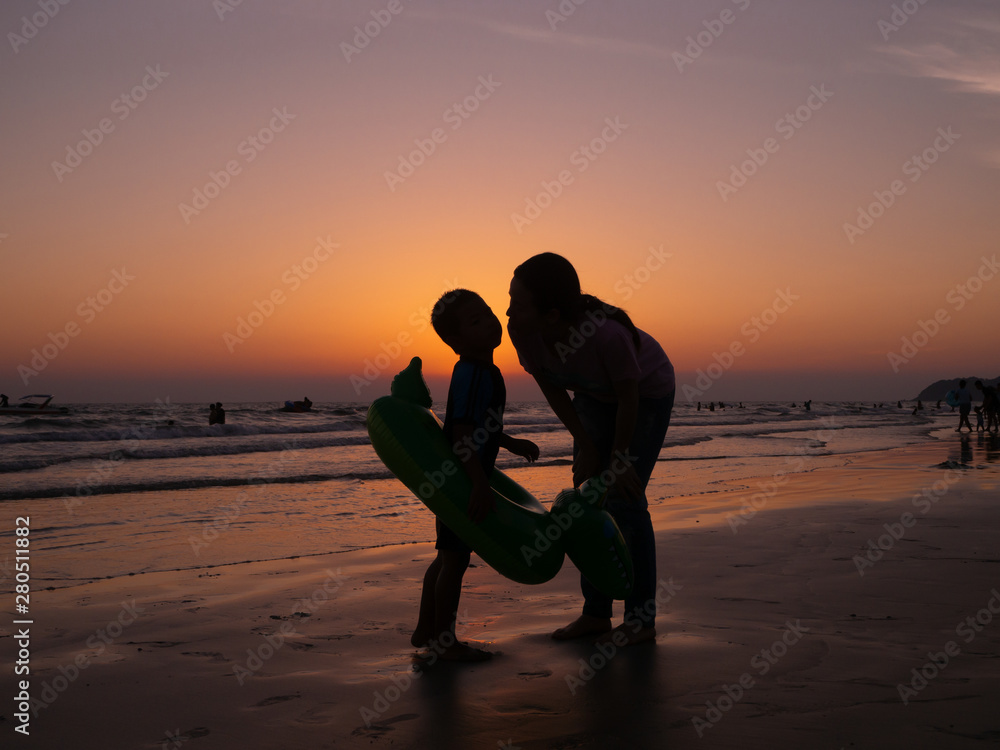 silhouette mother kissing son on beach with orange evening sky background, family lifestyle.