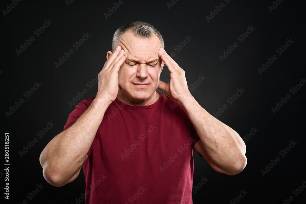 Handsome middle-aged man suffering from head ache on dark background Handsome middle-aged man suffering from head ache on dark background
