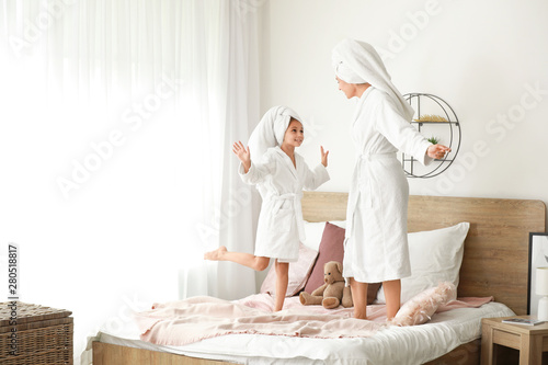 Mother and her little daughter in bathrobes having fun at home