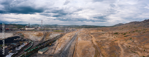 Train moving forward among the black dumps, polluted terrain, no vegetation; terrible landscape with anthropogenic influence of people on nature; transportation system of obsolete plant; aerial view