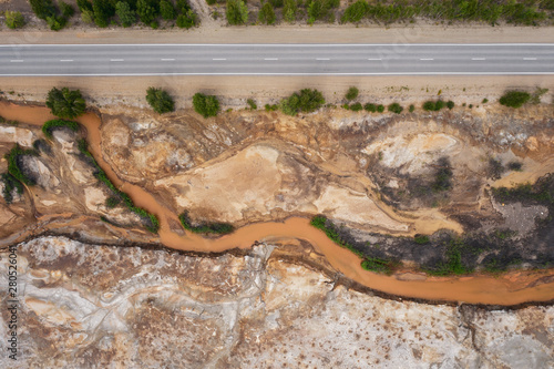 Aerial top down view; drone flying over a very polluted river with copper colored water; dumping of chemical waste into the river; dead vegetation, tree stumps; concept of environmental pollution