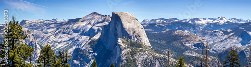 Panoramic view of the majestic Half Dome and the surrounding wilderness area with mountain peaks and ridges still covered by snow; Yosemite National Park, Sierra Nevada mountains, California