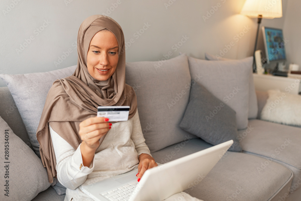 Arab woman making online purchase on laptop, ordering. Portrait of happy Muslim woman purchasing product via online shopping. pay using credit card. Gorgeous young woman using laptop shopping online. Arab woman making online purchase on laptop, ordering. Portrait of happy Muslim woman purchasing product via online shopping. pay using credit card. Gorgeous young woman using laptop shopping online.
