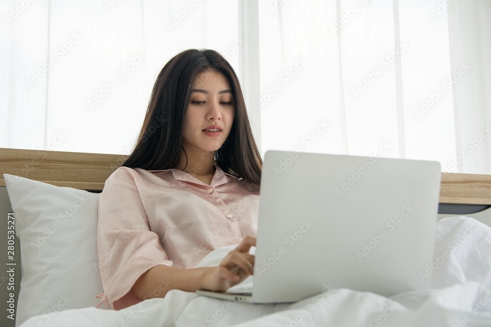 Portait of smiling lady in pink pajama wake up searching information in notebook on the bed Portait of smiling lady in pink pajama wake up searching information in notebook on the bed
