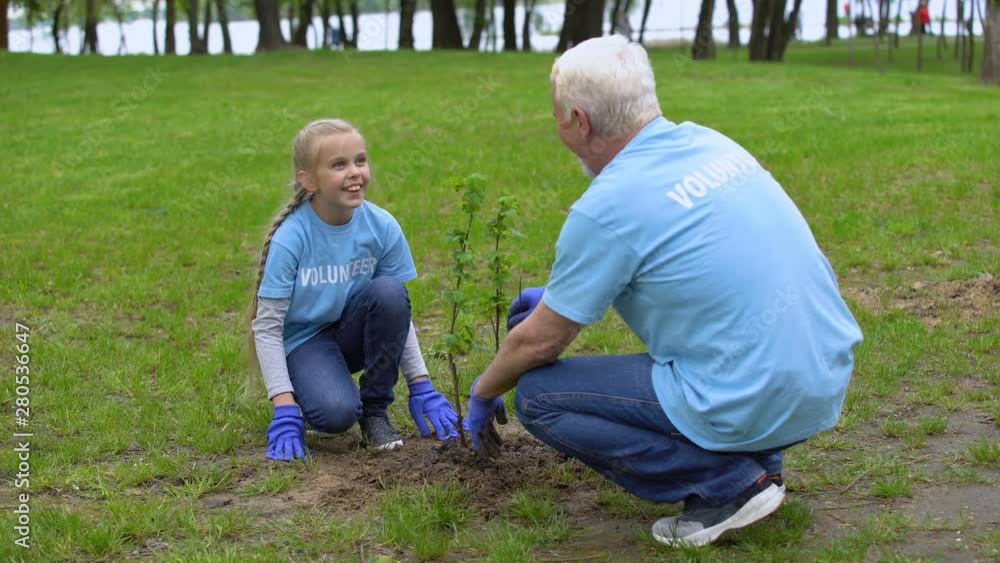 Happy senior volunteer and smiling female kid planting tree together, ecology Happy senior volunteer and smiling female kid planting tree together, ecology