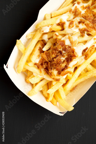 French fries with cheese sauce and onion in a paper box on a black background, top view. Flat lay, overhead, from above. Close-up.