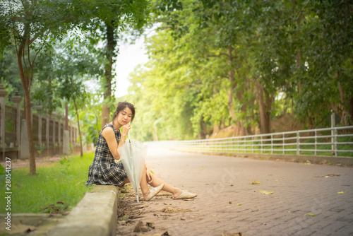 Lonely asian woman teenage in casual dress sit by walkway with big smile hand hold umbrella in public park and copy space. process in vintage style