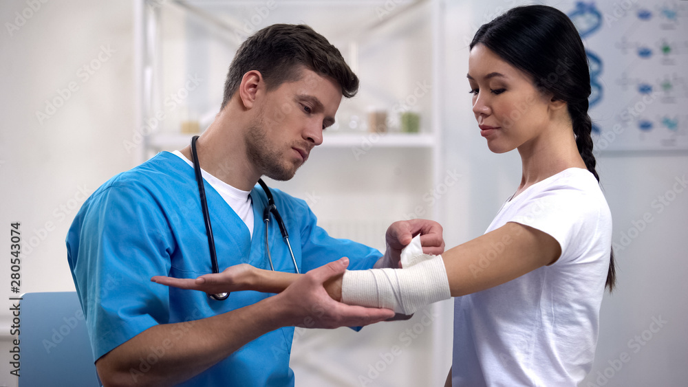Attentive therapist fixing elbow elastic warp female patient after injury health Attentive therapist fixing elbow elastic warp female patient after injury health