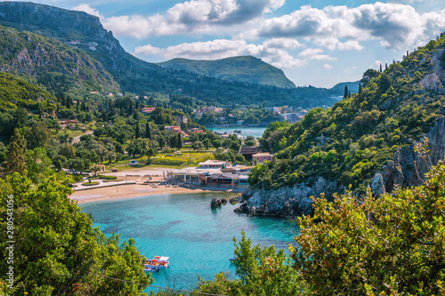 Beautiful landscape with sea–lagoon, beach, mountains and cliffs, green trees and bushes, rocks in a blue water, blue sky and clouds. Corfu Island, Greece. 