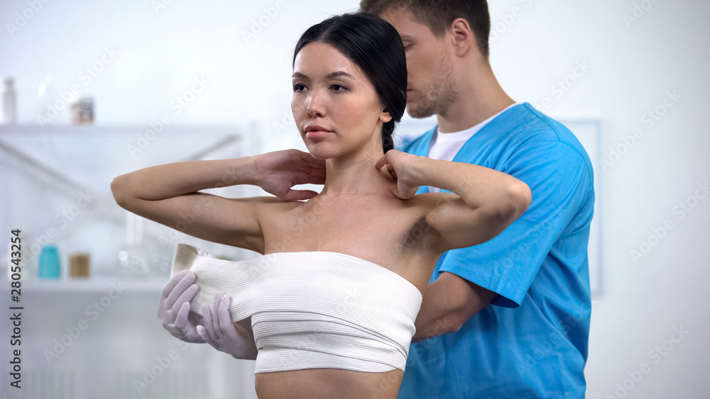 Male plastic surgeon applying elasto-fit breast female patient, compression