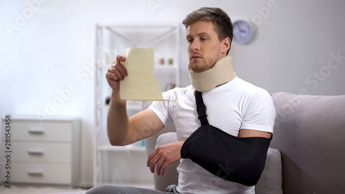 Male in foam cervical collar and arm sling reading prescriptions from doctor photo