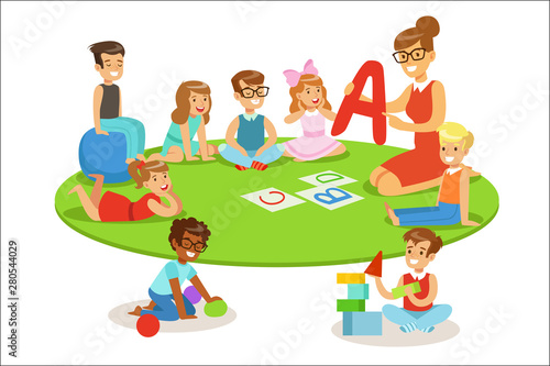 Young Children Learning Alphabet And Playing In Nursery School With Teacher Sitting And Laying On The Floor