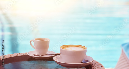 A cup of cappuccino and coffee on the background of emerald pool water.