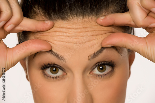 young woman pinching her forehead wrinkles with her fingers on a white background