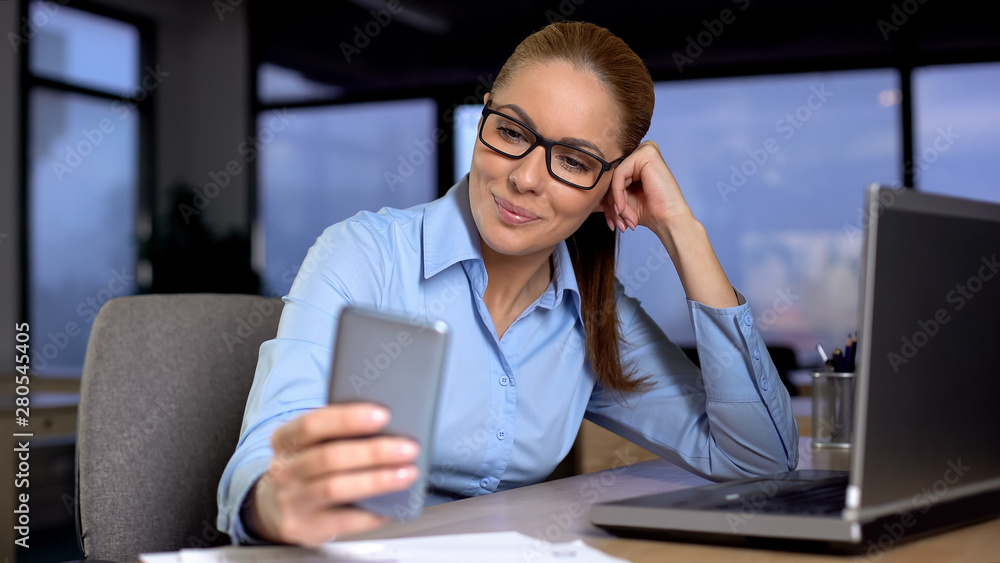 Woman typing message on mobile phone instead of working, bored at unloved job Woman typing message on mobile phone instead of working, bored at unloved job