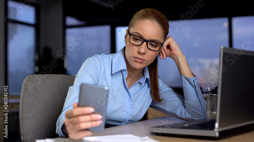 Tired woman checking time on smartphone, waiting to finish work, exhaustion