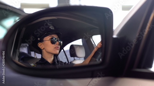 Serious police woman in sunglasses driving car, view from car mirror, order