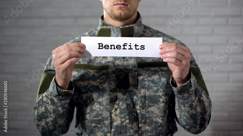 Benefits word written on sign in hands of male soldier, veterans support, aid photo