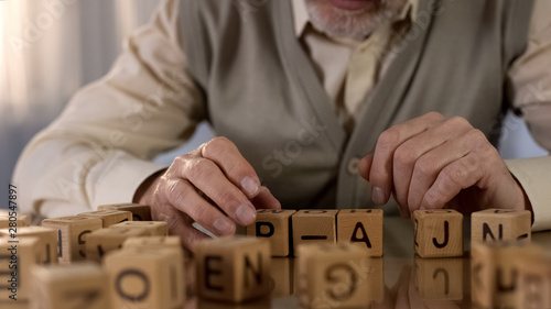 Male pensioner trying to make word of wooden cubes, old age dementia, rehab photo