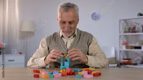 Bild auf Leinwand Positive old man playing with wooden cubes, cognitive training in Alzheimer
