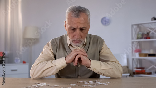 Obraz na plátně Old man exercises with puzzle, suffers cognitive impairment, Alzheimer symptom