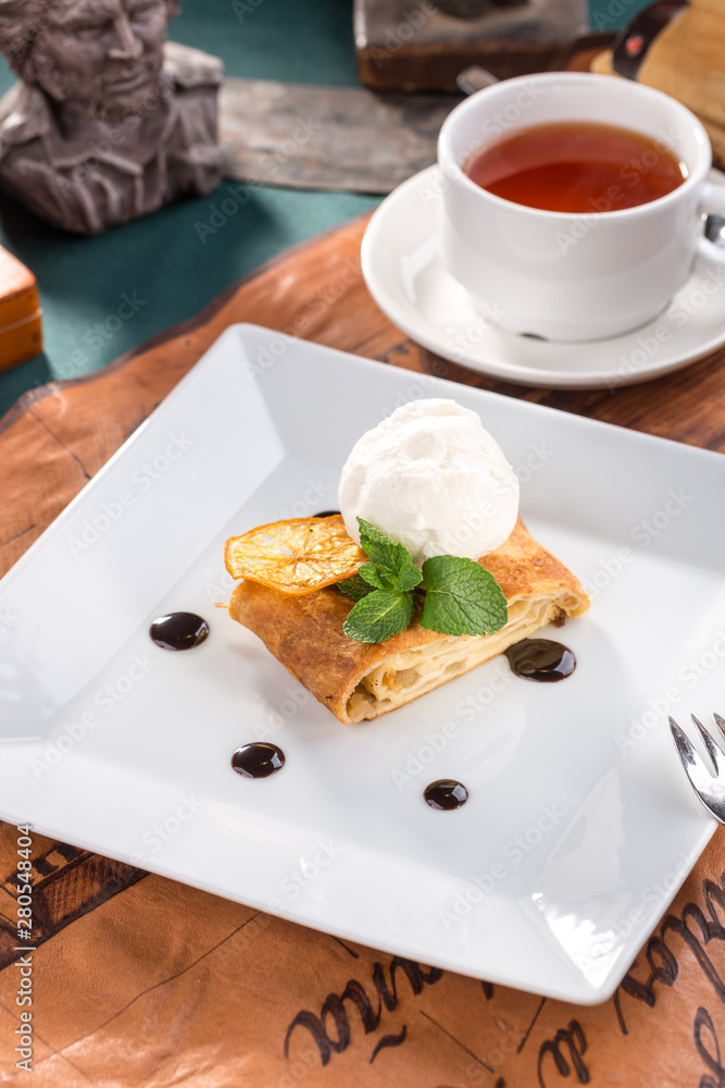 Freshly baked apple strudel with vanilla ice cream and mint and cup of tea on old map background