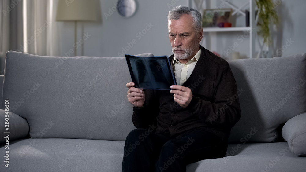 Old man sadly looking at x-ray image, difficulty coping with terminal diagnosis Old man sadly looking at x-ray image, difficulty coping with terminal diagnosis