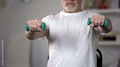 Фотография Old man lifting dumbbells, training muscles and joints after injury or insult