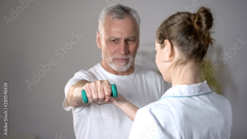 Fotografia Nurse helping old man to lift dumbbell, cardiac rehabilitation, injury recovery