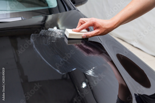 The process of applying a nano-ceramic coating on the car's hood by a male worker with a sponge and special chemical composition to protect the paint on the body from scratches, chips and damage.