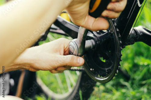 A man repairs a chain on a mountain bike with a socket wrench on the grass.