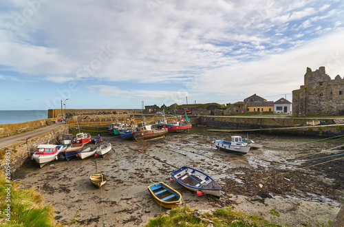 Fishing Boats lie on the silt at low tide in the inner harbour of Slade Village, overlooked by the Castle and ruins. Slade, County Wexford, Southern Ireland.