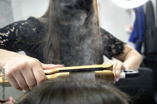 Cute girl with long brunette hair hairdresser doing hair lamination in a beauty salon. concept of hair care treatment, steam from hair