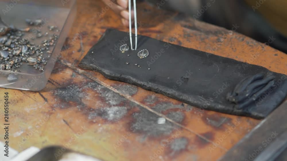 Craftsman is in a workshop for jewelry making.He is using forceps to work out a detail Craftsman is in a workshop for jewelry making.He is using forceps to work out a detail