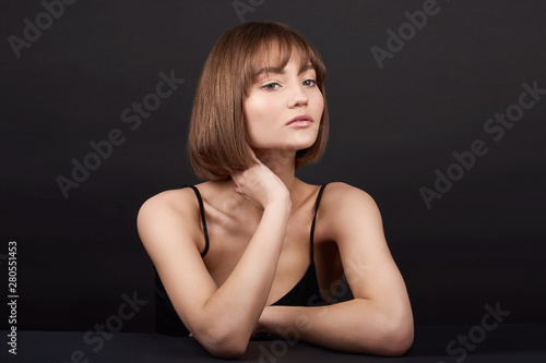 Beauty portrait of a beautiful young smiling girl with beautiful glowing skin and natural makeup on a black background in a black dress.