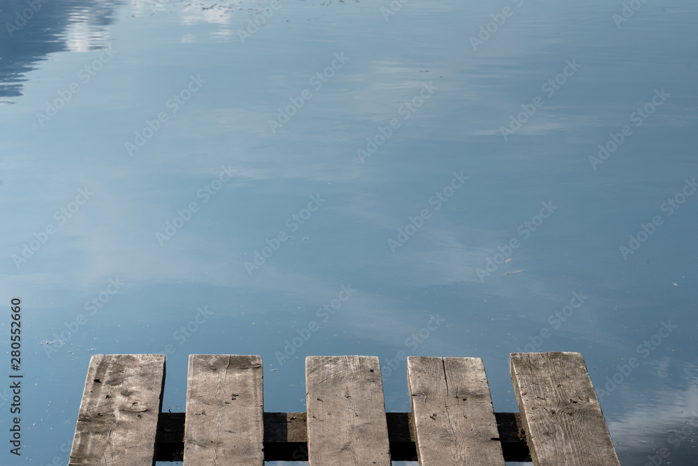 Fragment of a small wooden jetty on the background of the lake. Reflection of the sky in the lake.