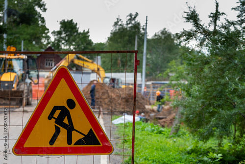 Road works sign on defocused background of workers and construction equipment