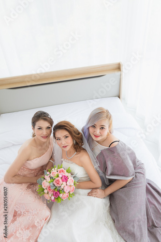 Asian bride and bridesmaids sitting on bed..