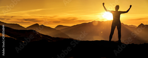 Frau in Siegerpose bei Sonnenaufgang auf einem Berggipfel