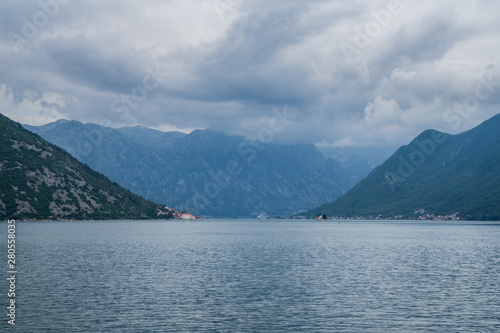 Montenegro, Majestic mountains surrounding fjords and island next to old town of perast village in kotor bay on cloudy day © Simon