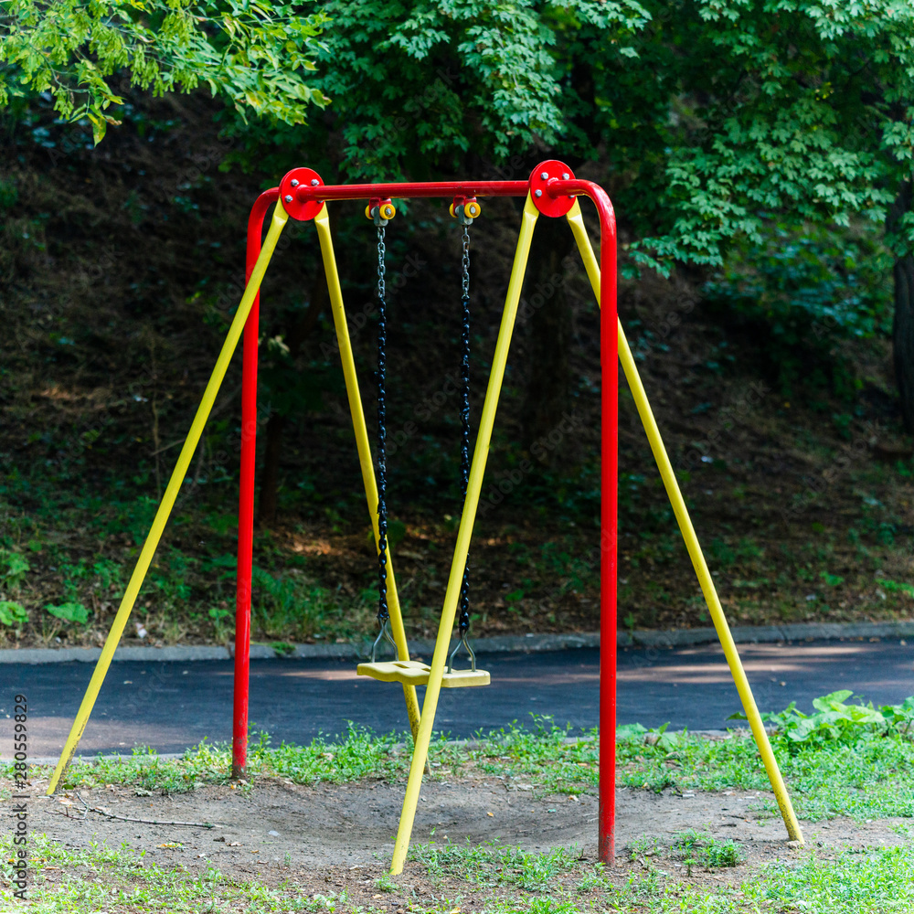 Fototapeta premium Children's swings hang empty an idle at a playground on a dull, overcast day