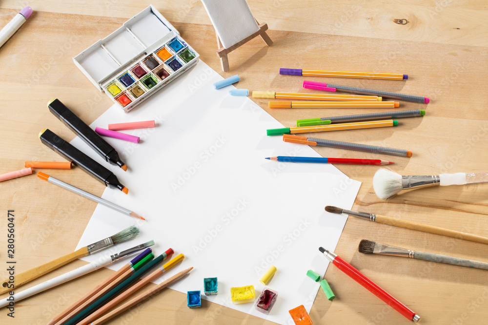 background with a set of watercolor paints, pencils, brushes and sheets of paper on a wooden table background with a set of watercolor paints, pencils, brushes and sheets of paper on a wooden table