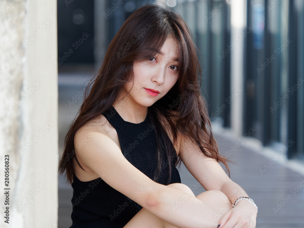 Graceful young woman with long black hair sitting on ground and leaning on the wall in sunny day. Outdoor portrait of cool Chinese girl in trendy summer sexy black dress and sandal, summer concept. Graceful young woman with long black hair sitting on ground and leaning on the wall in sunny day. Outdoor portrait of cool Chinese girl in trendy summer sexy black dress and sandal, summer concept.