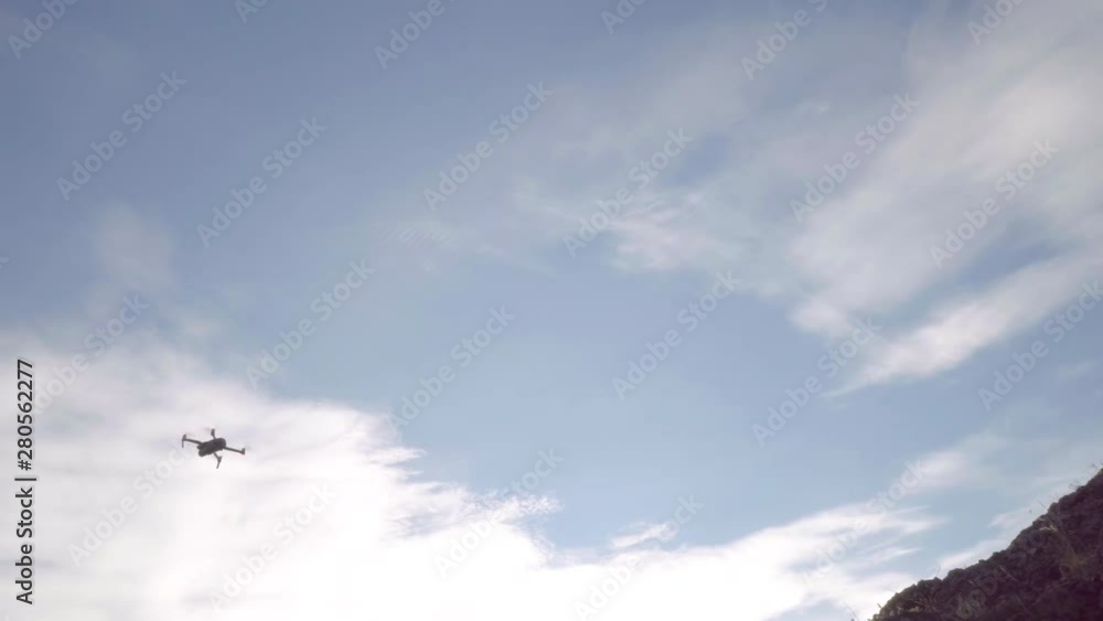 Handheld shooting of a flying drone. In the frame are tree branches and rocks. Evening time filming.