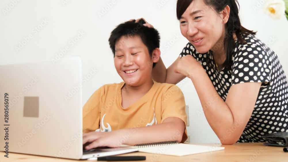 Asian mother looking after son doing homework on laptop at home. Asian mother looking after son doing homework on laptop at home.