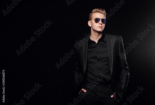 young man with black glasses in black jacket on black background
