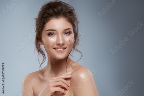 pretty girl with curly hairstyle and flowers on face smiling with naked shoulders