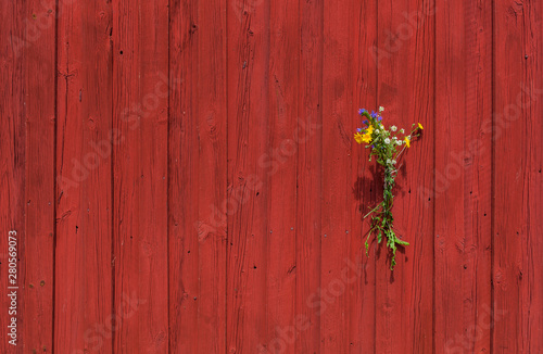 Blumenstrauß dekoriert rote Holzwand. Bouquet of flowers decorating red wooden wall.